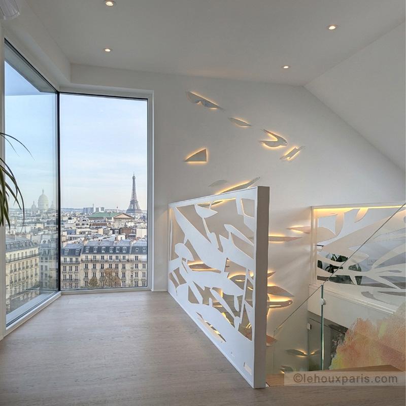 creation luminaire rampe d escalier design sculpturale Lehoux Paris, rampe d'escalier contemporaine et mobilier Roche Bobois dans un salon de duplex avec baie vitrée vue tour Eiffel.