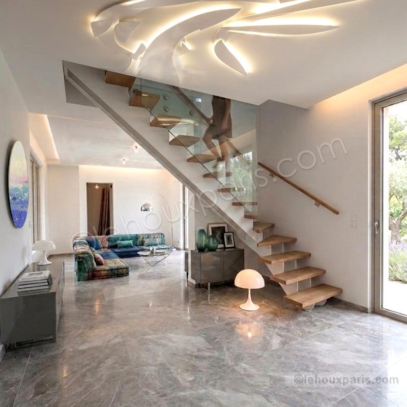 Suspension lumineuse sur mesure Lehoux Paris au plafond d'un salon avec canapé Roche Bobois. et tableau rond prisca temporal